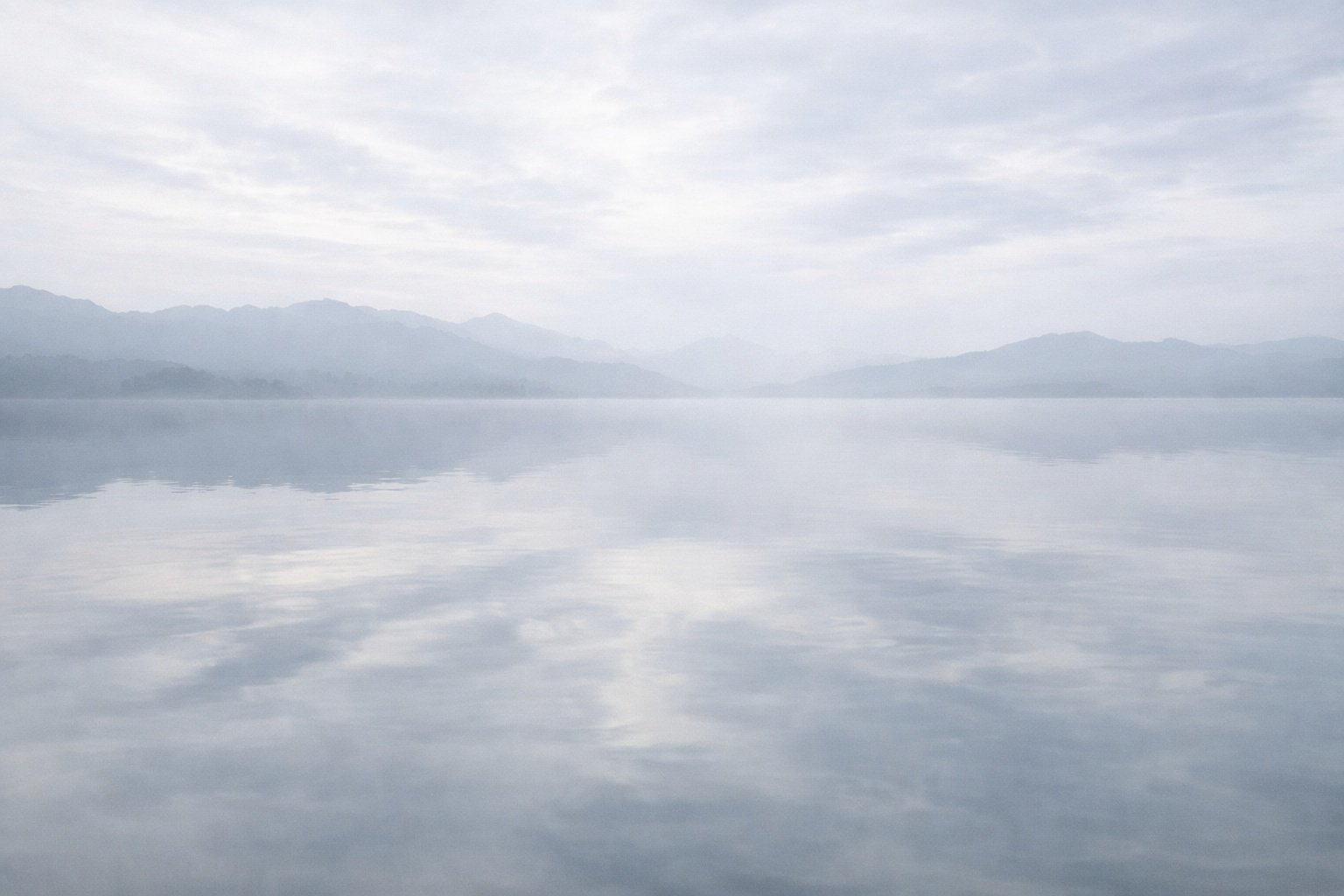 Still water reflecting sky and distant mountains in a minimal composition.